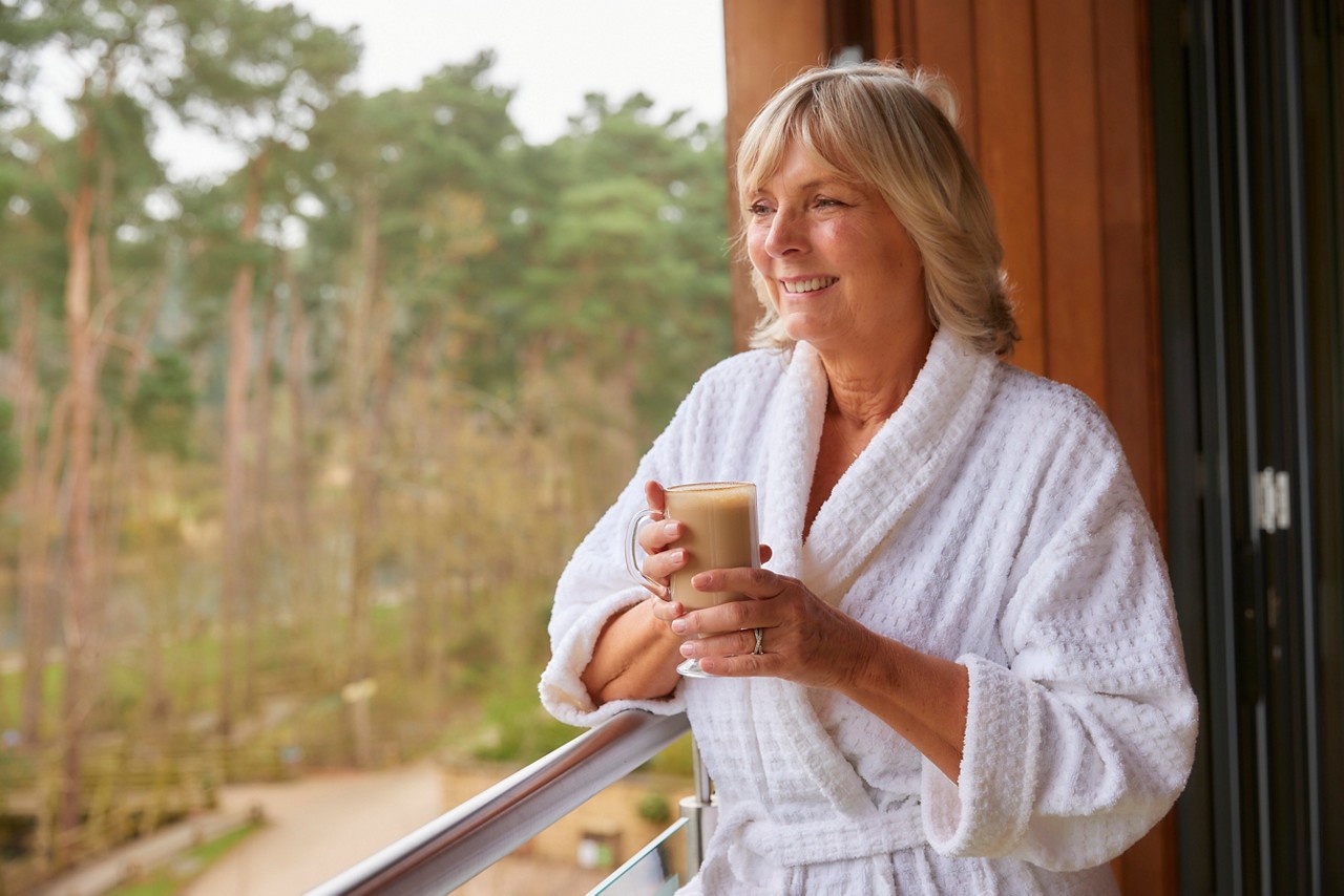 Woman drinking a coffee whilst looking out to the forest